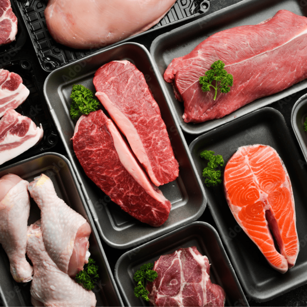 Various cuts of raw meat are displayed in black trays, including chicken drumsticks, beef steaks, and salmon fillets. Some trays are garnished with small sprigs of parsley. The meats are neatly arranged and appear fresh.