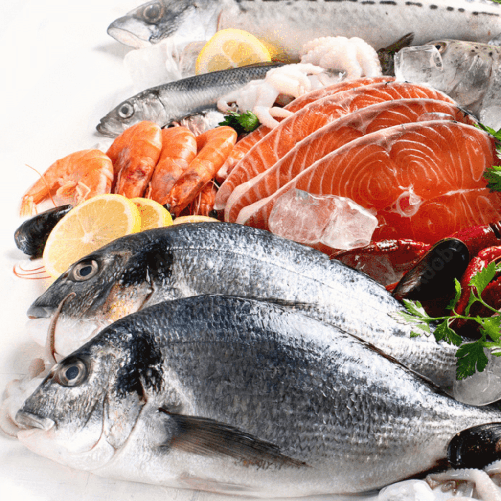 A selection of fresh seafood on ice, including whole fish, shrimp, salmon slices, and squid rings, garnished with lemon slices and parsley. The seafood assortment is arranged on a white surface.